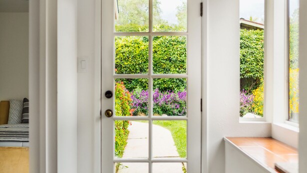 A white door with a glass panel, leading to a garden with various plants and flowers. - Coastal ranch-style home in garden setting.  (Carpinteria)