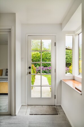 Une porte blanche avec un panneau de verre, qui donne sur un jardin où poussent différentes plantes et fleurs.