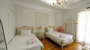 Quarto de hotel com duas camas de solteiro, um candelabro, um espelho e uma janela com cortinas.