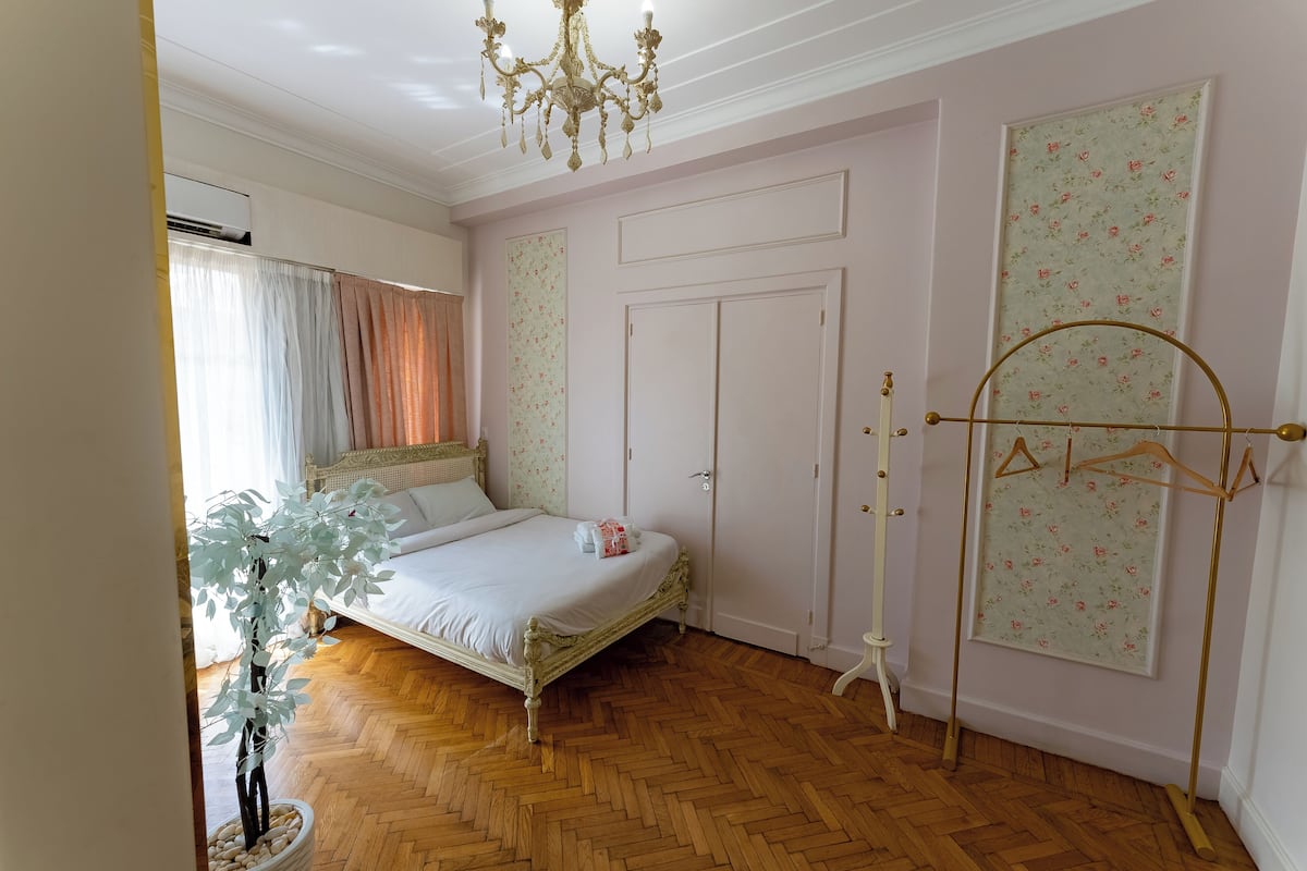 A bedroom with a bed, a wardrobe, a hanging clothes rack, and a potted plant.