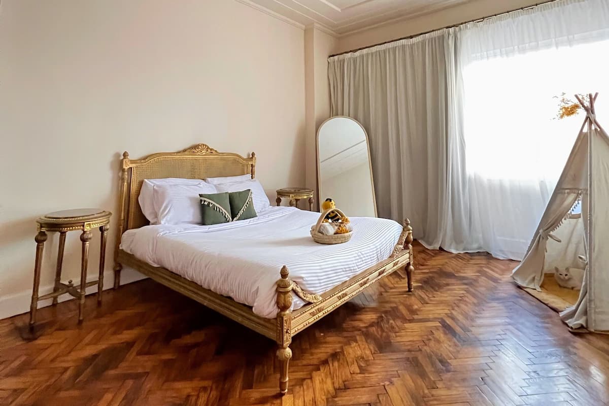 A neatly made bed with a wooden frame and white bedding, a round mirror on the wall, and a tent-like structure in the corner.