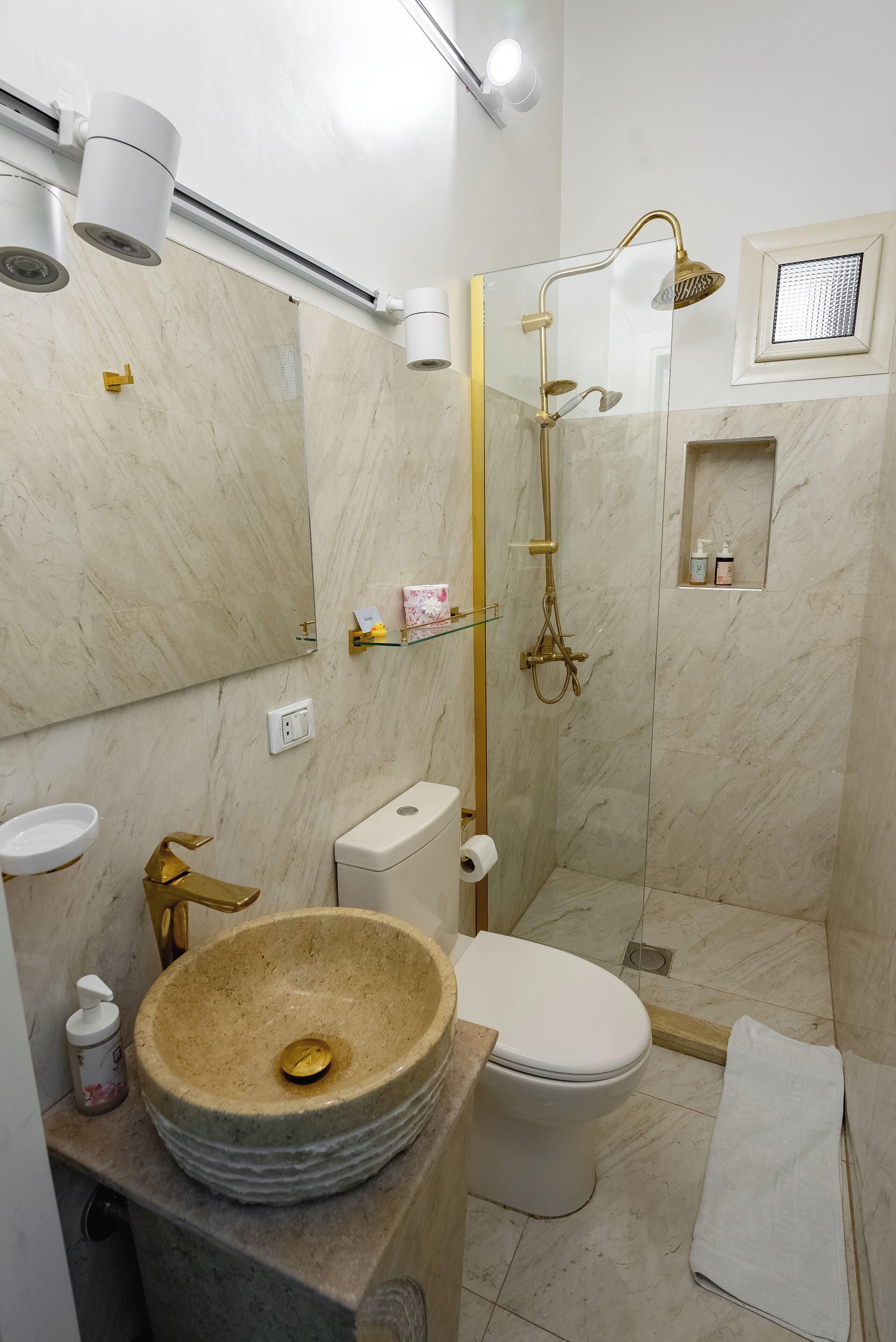 Een badkamer met een marmeren wastafel, toilet en een douche met glazen wanden.