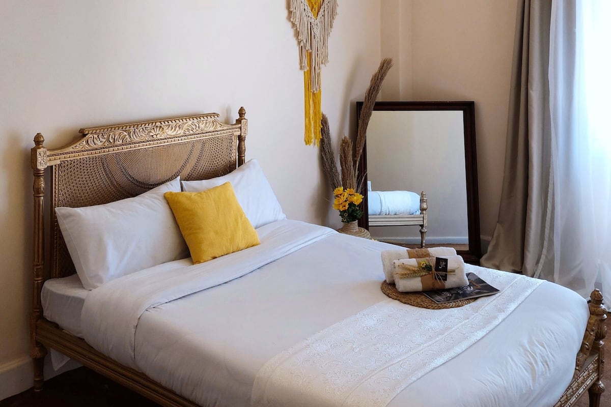 A neatly made bed with a wooden headboard, a yellow pillow, and a decorative tray with towels.