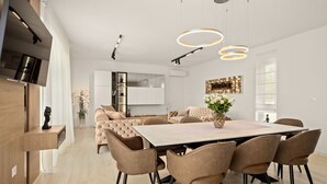 A modern kitchen with a central island, a dining area with a large table and chairs, and a living area with a sofa and decorative plants. - Vacation home Tea by Interhome (Pula)