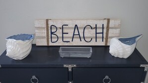 Musta metallipöytä, jossa on kaksi koristeellista simpukkaa ja metallinen alusta. Pöydän yläpuolella on puinen kyltti, jossa lukee sana ”BEACH”.