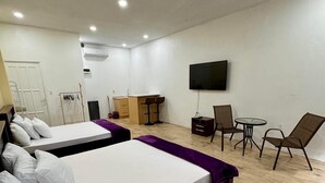A hotel room with two beds, a small kitchenette, a TV, and a seating area with chairs and a table.