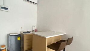 A compact kitchen with a white countertop, a sink, and a small refrigerator. There are two stools at the counter.