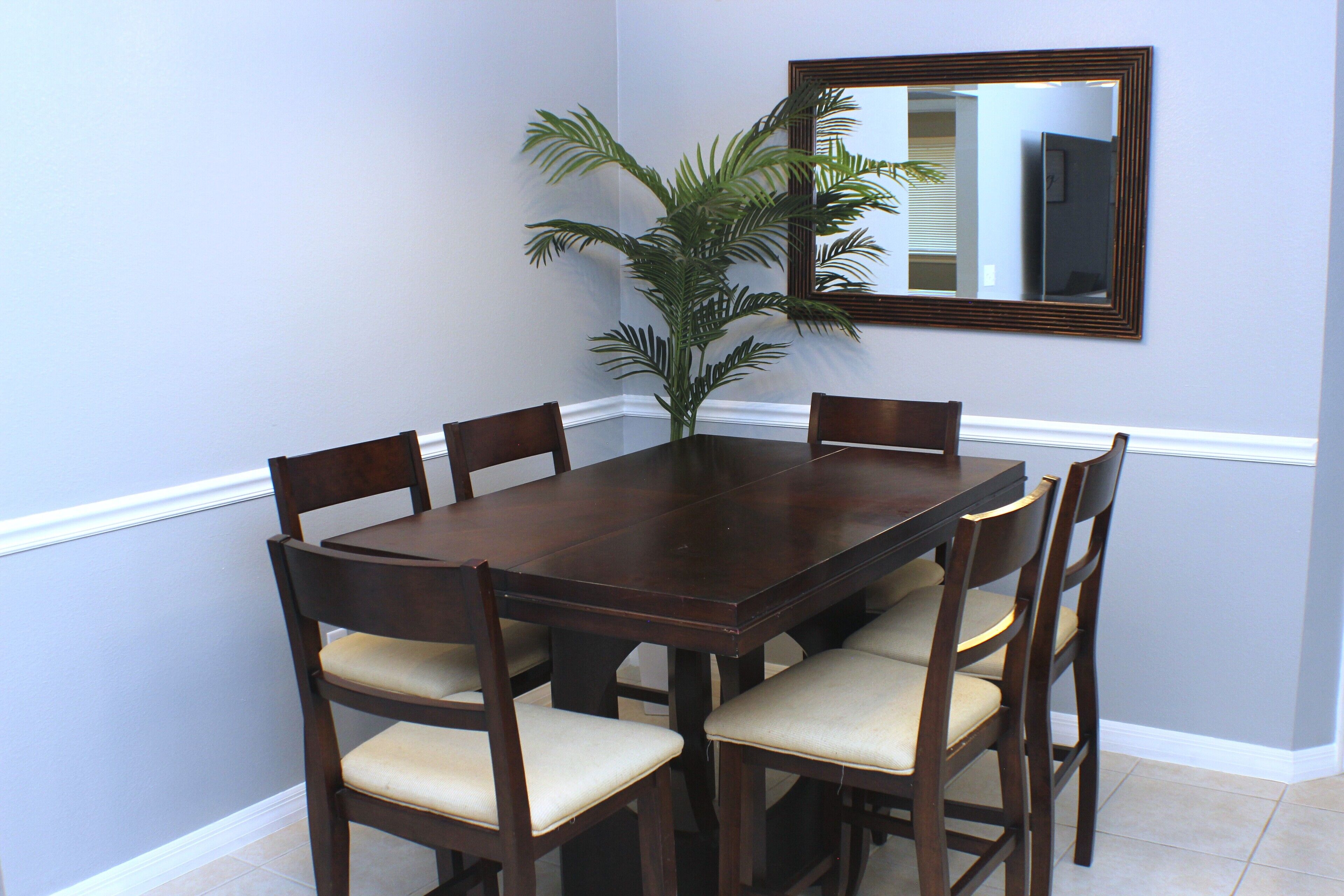 A dining table with six chairs, a potted plant, and a mirror on the wall.