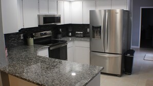 A modern kitchen with white cabinets, a stainless steel refrigerator, a microwave, and granite countertops. - Pool and Fishing Lake Oasis (Port Richey)