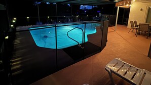 A swimming pool with a glass enclosure, a covered patio area with chairs, and a view of the sky. - Pool and Fishing Lake Oasis (Port Richey)