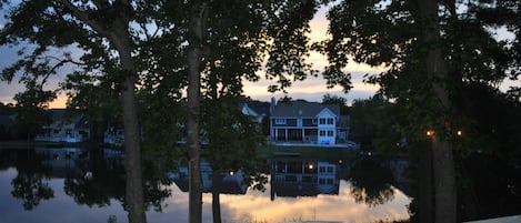 Blick auf einen See mit einer Holzterrasse, Bäumen und einem Haus, das sich im Wasser spiegelt.