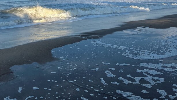 A beach with waves crashing onto the shore and a clear blue sky.
