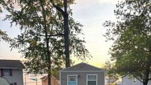 Een klein, gelijkvloers huis met een lichtblauwe deur en witte details, omringd door een verzorgd gazon en bomen.