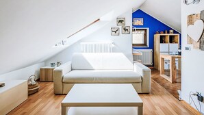 Et moderne loftværelse med skrå vægge, en hvid sofa, et træspisebord og en blå væg.