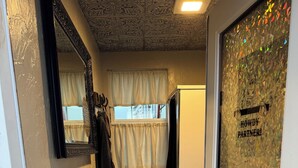 A bathroom with a checkered rug, a mirror, a towel rack, a shower curtain, and a door with a frosted glass window.