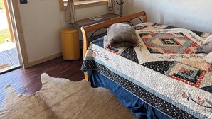 A room with a bed, a wooden headboard, a window with curtains, a wall-mounted coat rack, a framed picture, and a rug.