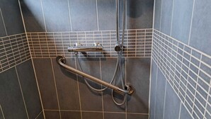 Ein Duschbereich mit Haltegriff, Handbrause und Toilette.