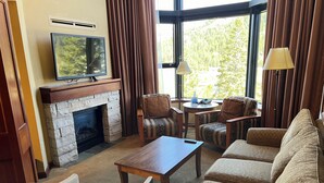 A living room with a stone fireplace, a television, two patterned armchairs, a sofa, a coffee table, and a lamp. - Everline Resort & Spa: Deluxe Two-Bedroom Penthouse
Ski In/Out, Golf, Spa, Pool (Olympic Valley)