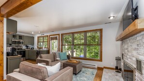 A modern living room with a fireplace, large windows, and a kitchen in the background.
