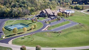 An aerial view of a hotel with a large parking lot, a tennis court, and a building with a prominent roof.