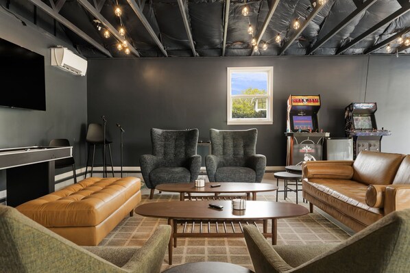 Un salón moderno con sofás de cuero, mesa de billar y juegos de arcade.
