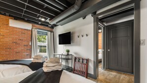 A modern hotel room with a large bed, a flat-screen TV, a small table with a plant, and a view of the outdoors. - Sauna & Hot Tub Chalet w/ Game Room, 6BR (Asheville)