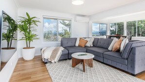 A modern living room with a grey sectional sofa, a white rug, and two potted plants. - Coastal Sanctuary with Ocean Views. (Tweed)