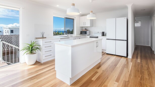 A modern kitchen with white cabinetry, a large island, and a view of the ocean. - Coastal Sanctuary with Ocean Views. (Tweed)