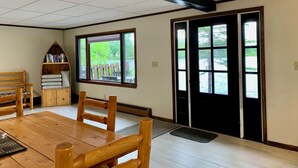 Una habitación con una mesa de madera, sillas, una estantería y un ventanal con vistas a la vegetación.