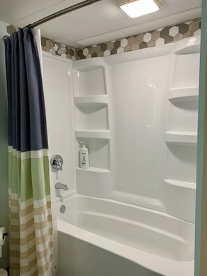 Un baño con bañera, cortina de ducha y una botella de champú Dove en la pared.