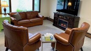 Una sala de estar con un sofá de cuero, dos sillones de cuero, un televisor, una chimenea y una ventana con vista a un lago.