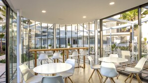 A modern indoor dining area with glass walls, white tables, and chairs.