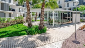 A modern apartment complex with a glass conservatory, palm trees, and a well-maintained garden.