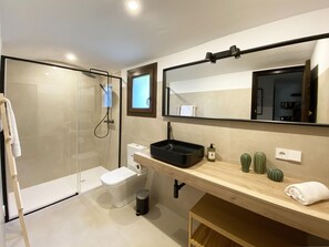 Ein modernes Badezimmer mit einer Duschkabine aus Glas, einer Toilette, einem Waschbecken mit schwarzem Becken und einem Spiegel über dem Waschbecken.