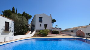 Ein weißes Gebäude mit Pool, umgeben von Bäumen und blauem Himmel.