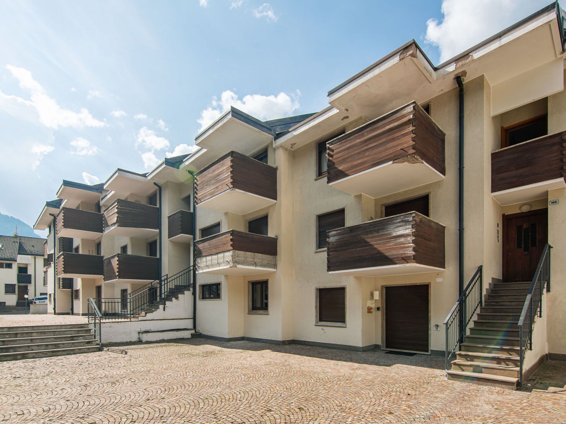Een rij moderne meerlaagsgebouwen met balkons, een geplaveid binnenterrein en een heldere lucht.