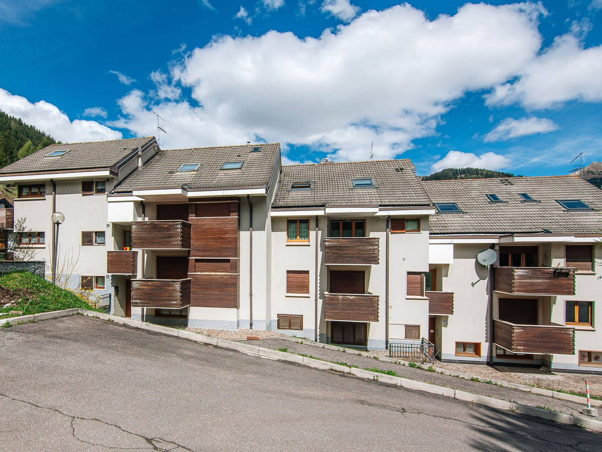 Une rangée d’immeubles résidentiels modernes à plusieurs étages, dotés de balcons et d’antennes paraboliques, se dressant sous un ciel bleu azur.