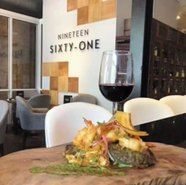 Interior de restaurante com mesa posta para refeição, uma taça de vinho e um quadro de menu.