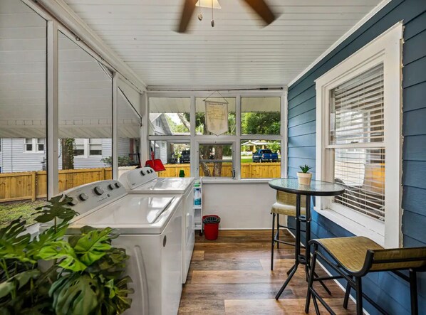 A laundry area with a washer and dryer, a small table, and a window overlooking a backyard.