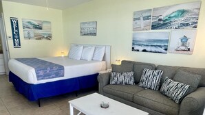 Una habitación con una cama, un sofá y una mesita de café. Incluye decoración en las paredes, como un cartel de 'Welcome' y fotografías del océano.