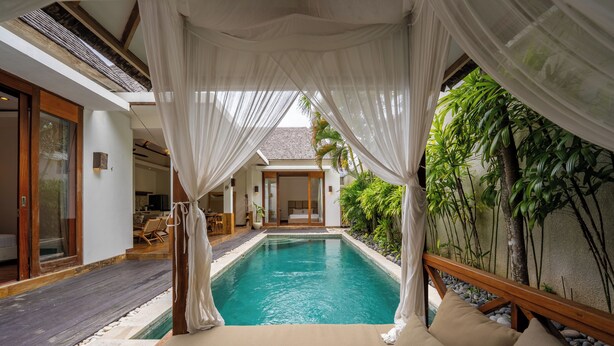 A serene pool area with a wooden deck, a cushioned seating area, and lush greenery. - Villa Chloe by Pertama Stay (Seminyak)