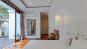 A bedroom with a large bed, a mirror, a chair, and a view of the outdoors. - Villa Chloe by Pertama Stay (Seminyak)
