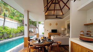 A wooden dining table with chairs, a pool, and a living area with a sofa and TV. - Villa Chloe by Pertama Stay (Seminyak)