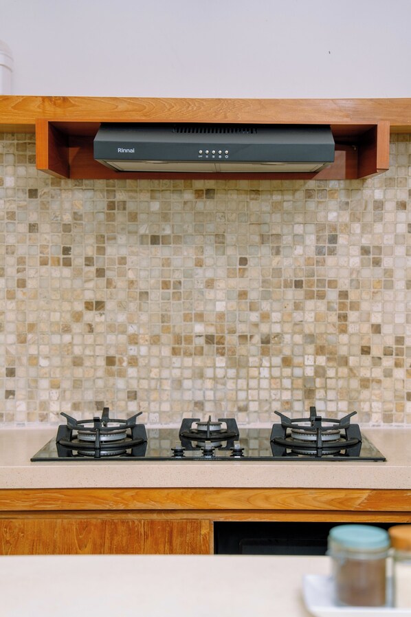 A kitchen with a gas stove, a Rinnai range hood, and a tiled backsplash. - Villa Chloe by Pertama Stay (Seminyak)