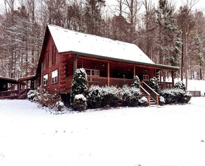 Una cabaña de troncos con un porche, rodeada de árboles cubiertos de nieve.