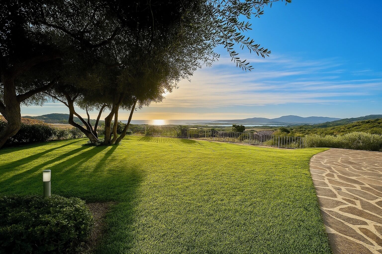 Ein gepflegter Rasen mit einem gepflasterten Weg und einem Zaun, mit Blick auf eine malerische Landschaft mit Hügeln und blauem Himmel.