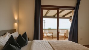 A hotel room with a bed, a nightstand, a lamp, a balcony with chairs, and a view of the sea.
