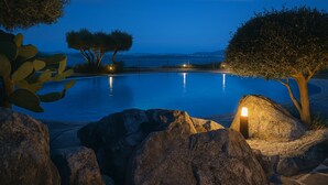 A nighttime pool area with a view of the sea, surrounded by rocks and trees.