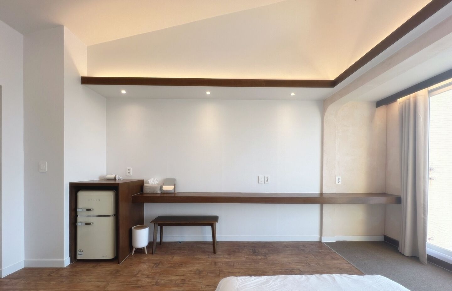 Un dormitorio moderno con suelo de madera, una cama, un escritorio con silla y un pequeño armario.