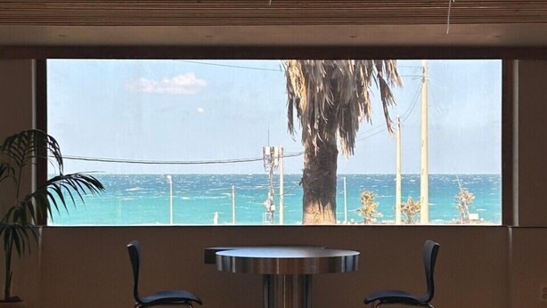 A room with a large window offering a view of the ocean and palm trees. There are two chairs and a table in the room. - Gongzonestay (Jeju City)